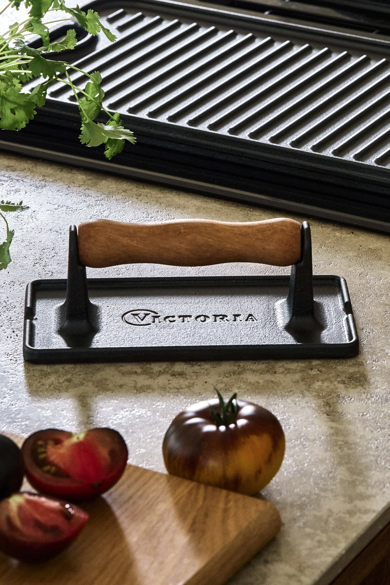 Keittiön sivupöydällä tomaattien ja paistinpannun vieressä oleva valurautainen lihapuristin. 