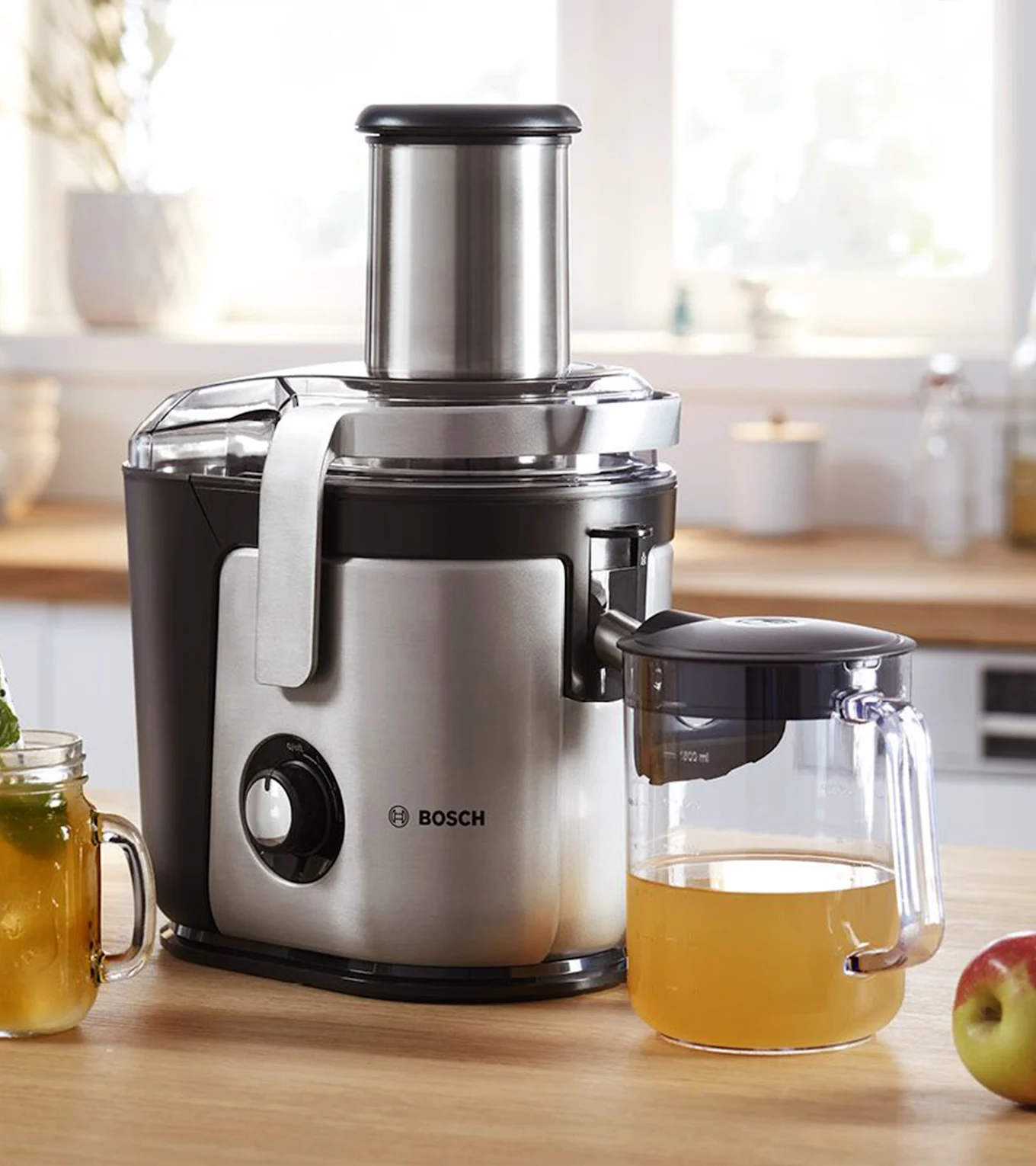 Hopeanvärinen ja musta Bosch-mehustin keittiötasolla, jossa kannu omenamehua ja omena.