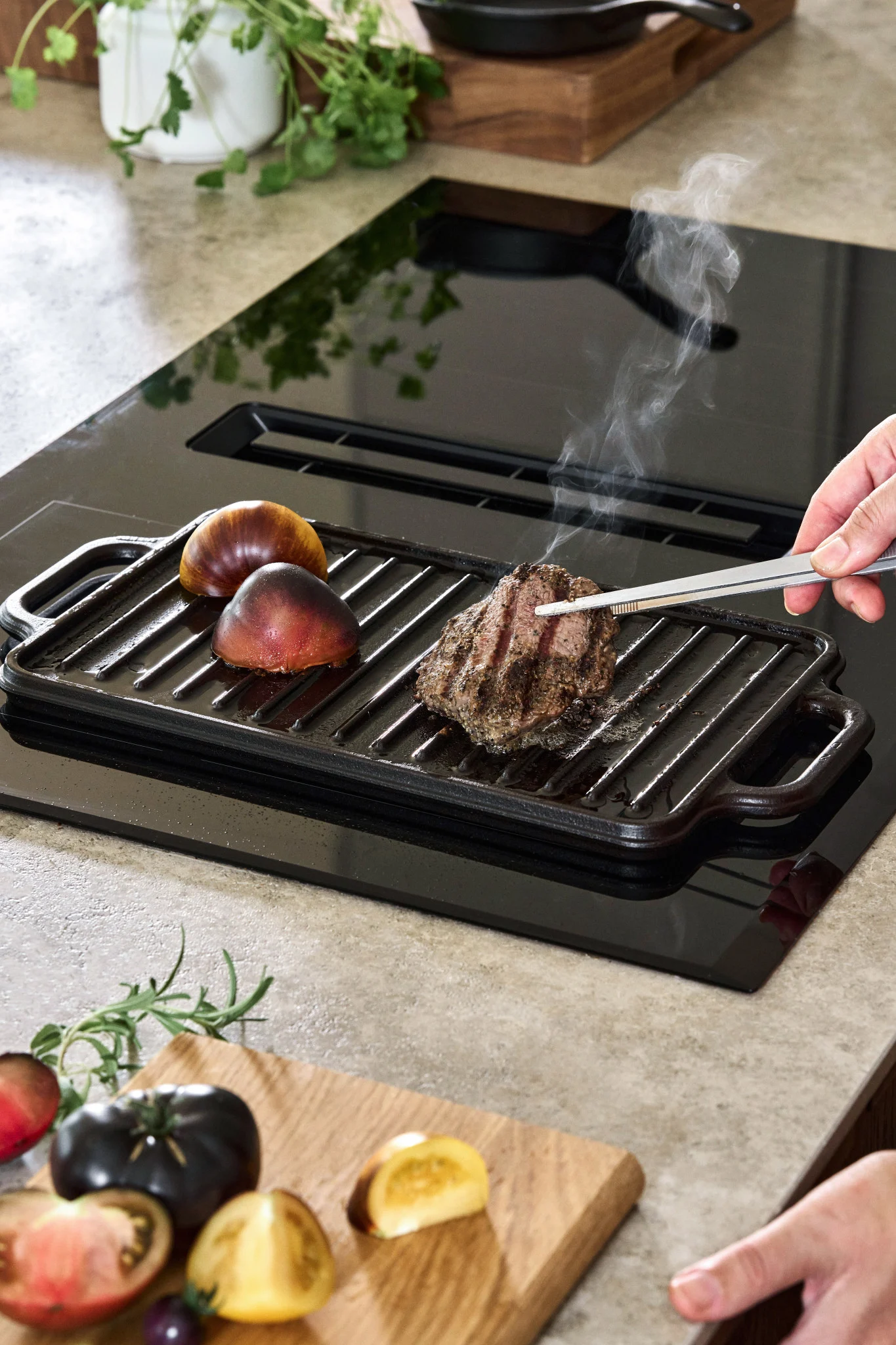 Valurautapannu induktioliedellä, jossa on pari tomaattia ja pala pihviä. 