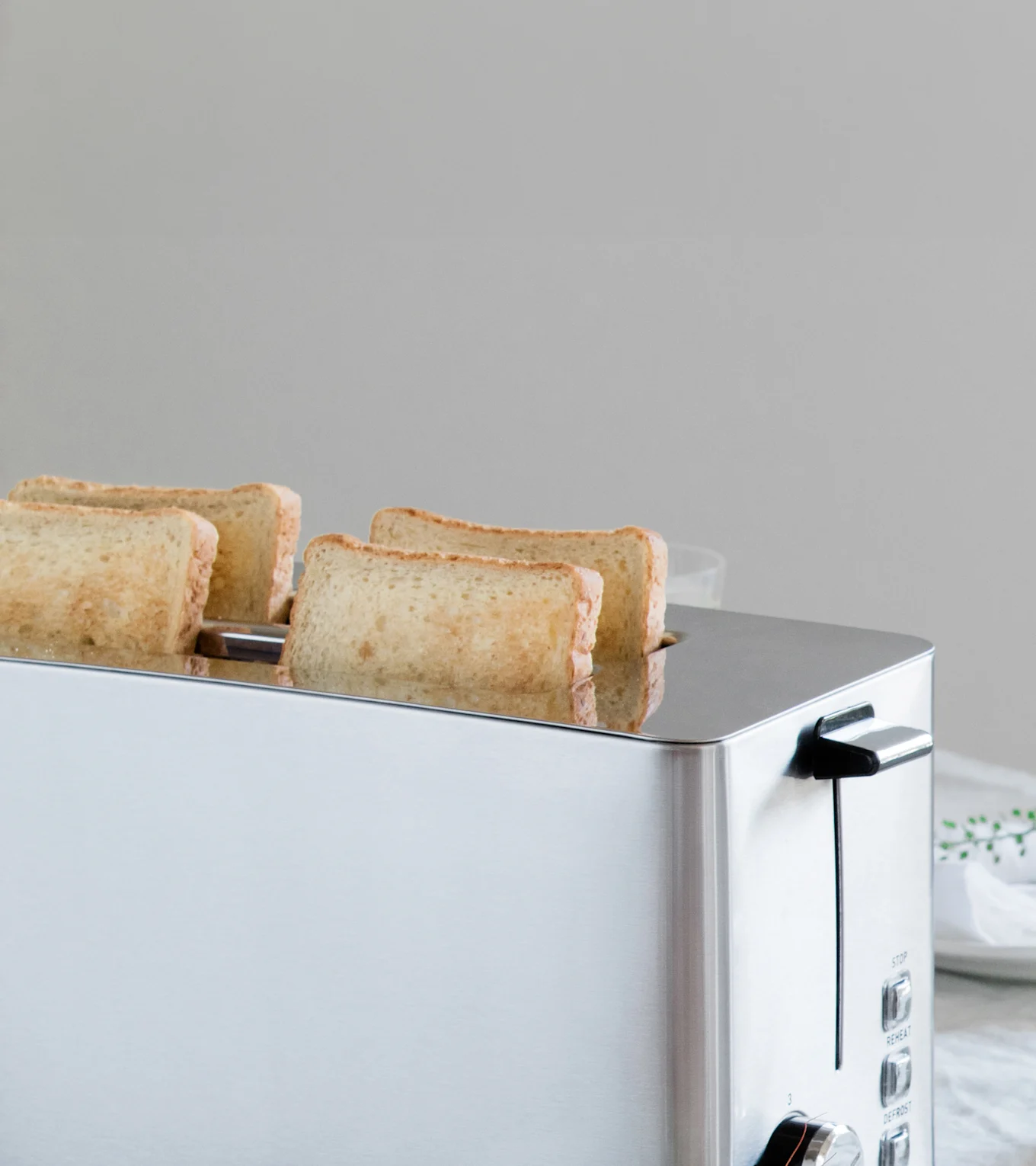 Hopeinen leivänpaahdin, jossa neljä kevyesti paahdettua leipäviipaletta nousee osittain aukoista.