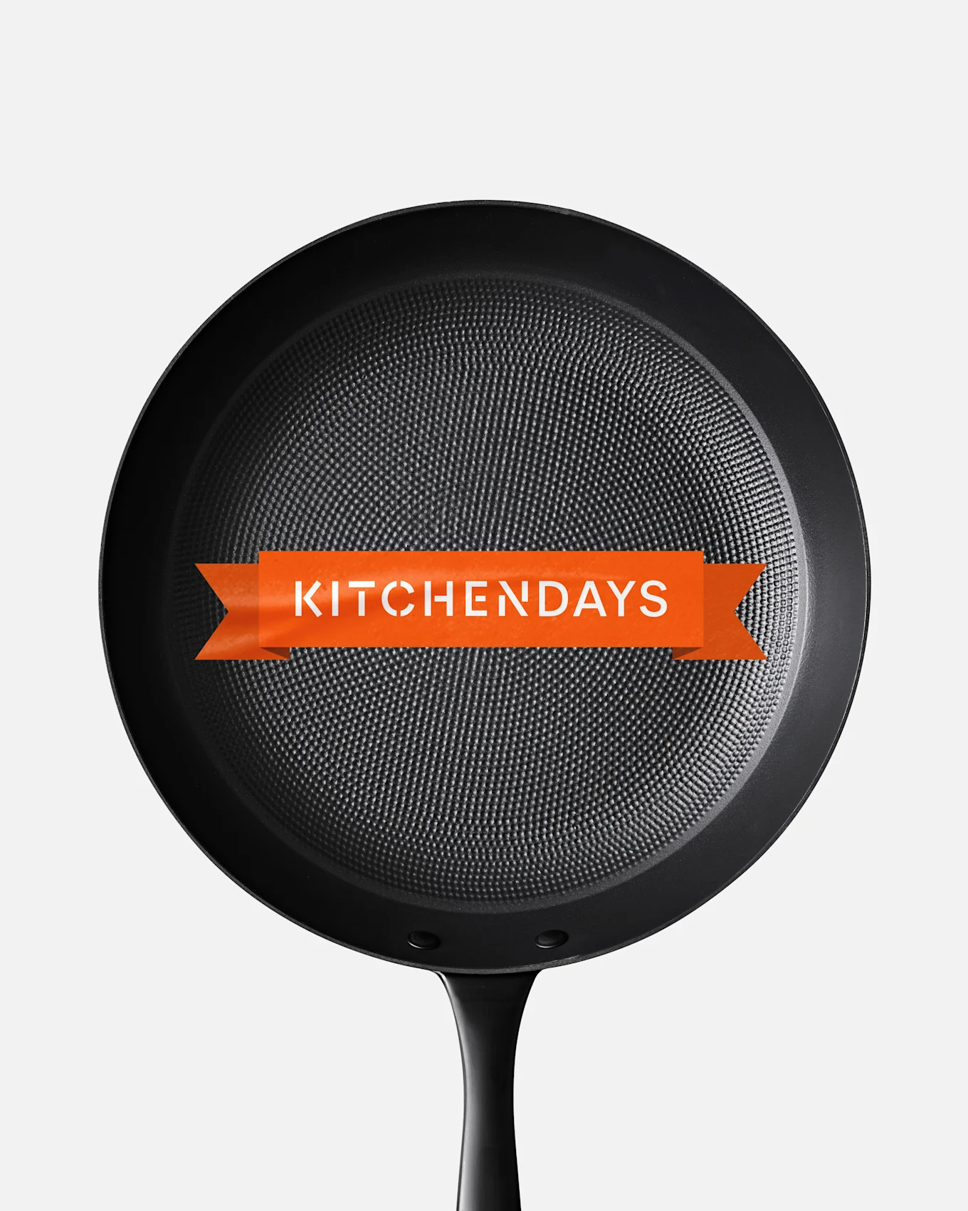 Musta paistinpannu kuvioidulla pinnalla ja oranssi banneri keskellä, jossa lukee 'KITCHENDAYS'.