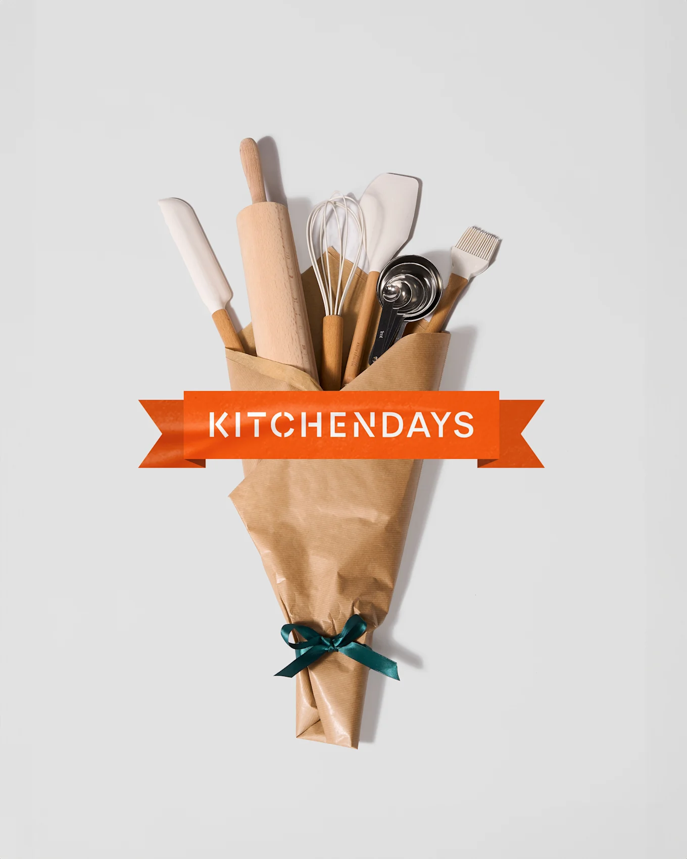 Ruskeaan paperiin kääritty keittiövälinekimppu vihreällä nauhalla ja oranssilla bannerilla 'KITCHENDAYS'.