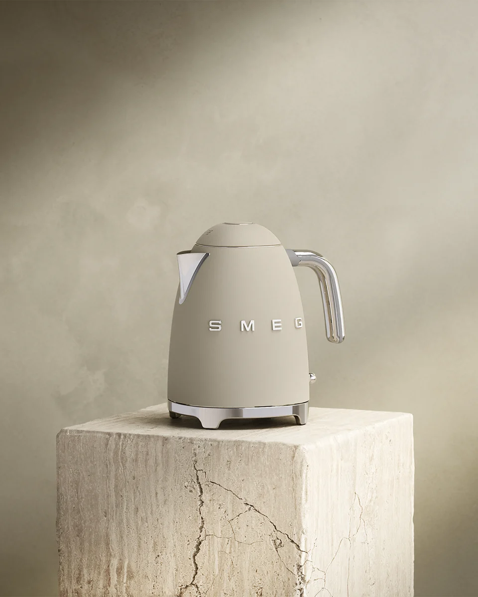 Beige Smeg-vedenkeitin kromiyksityiskohdilla teksturoitulla kivijalustalla.
