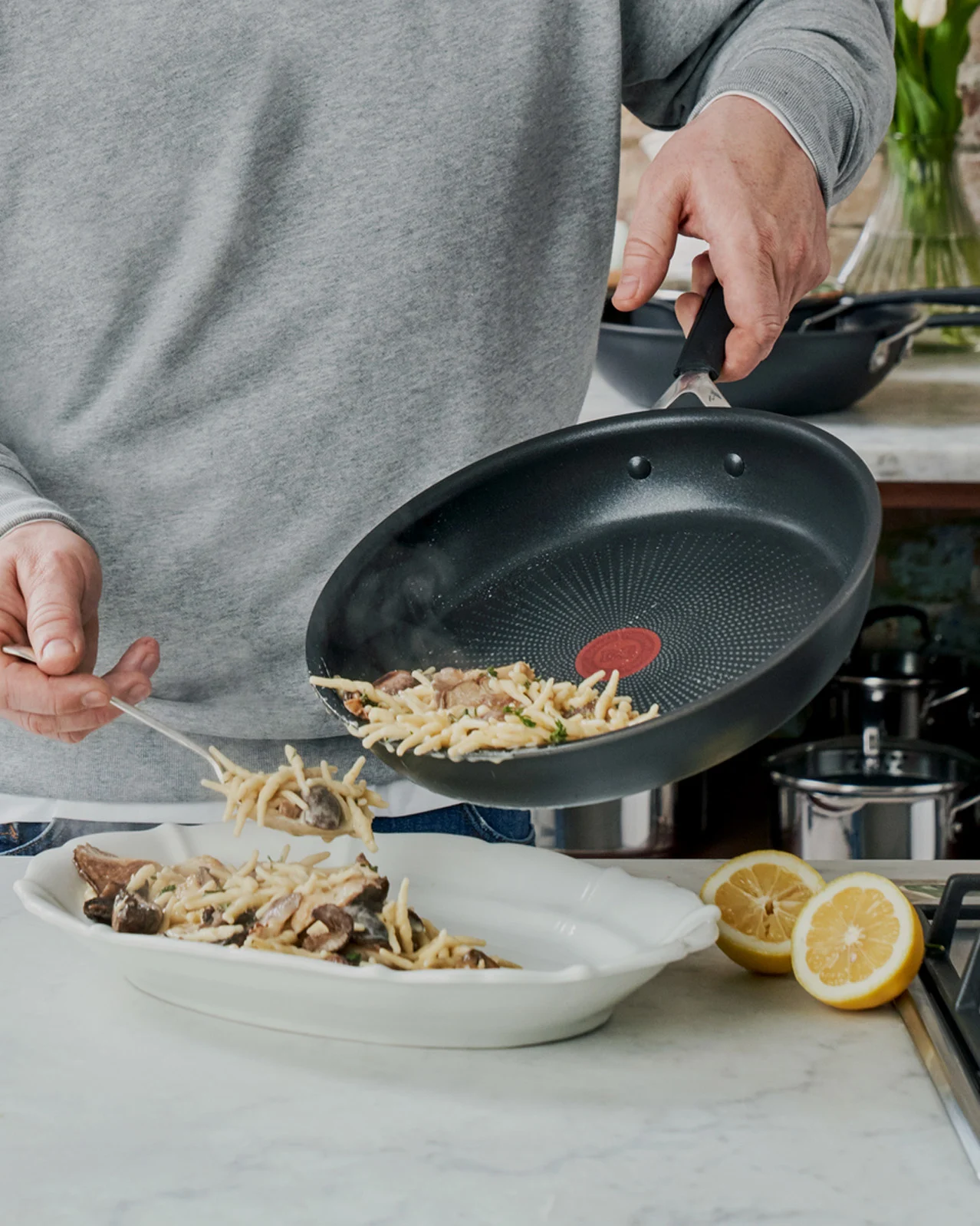 Henkilö annostelee sieni-pastaa paistinpannulta tarjoiluastiaan.